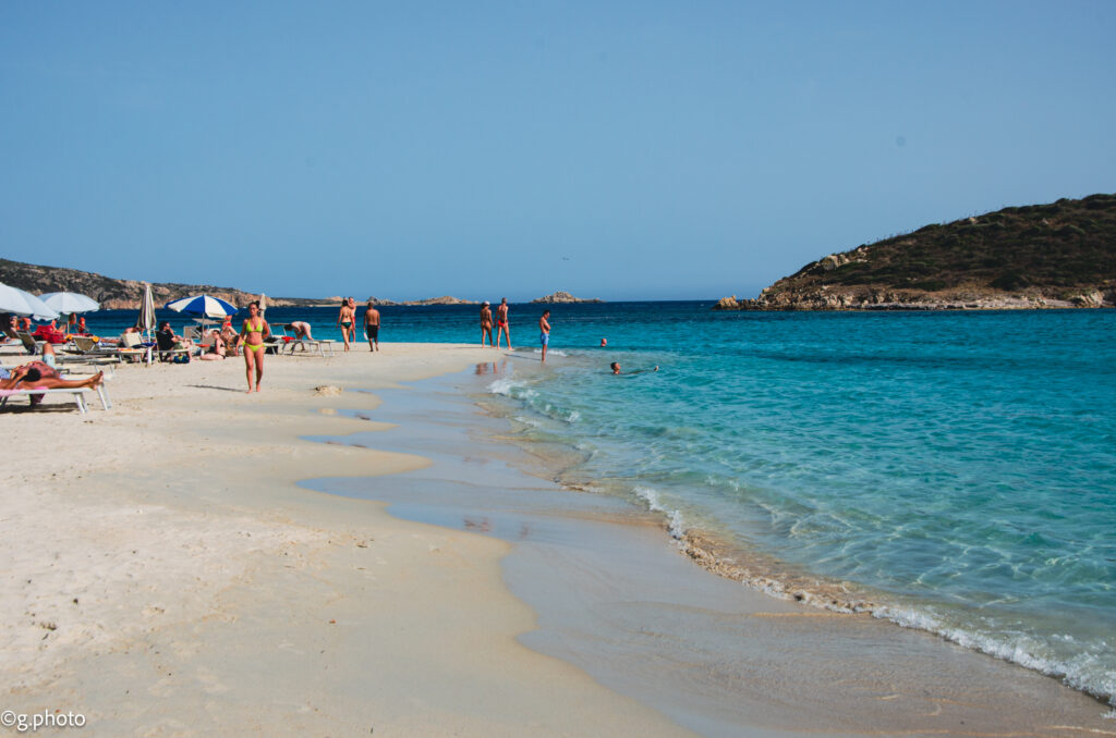 Spiaggia di Cala Tuerredda con bagnanti e promontorio roccioso sullo sfondo