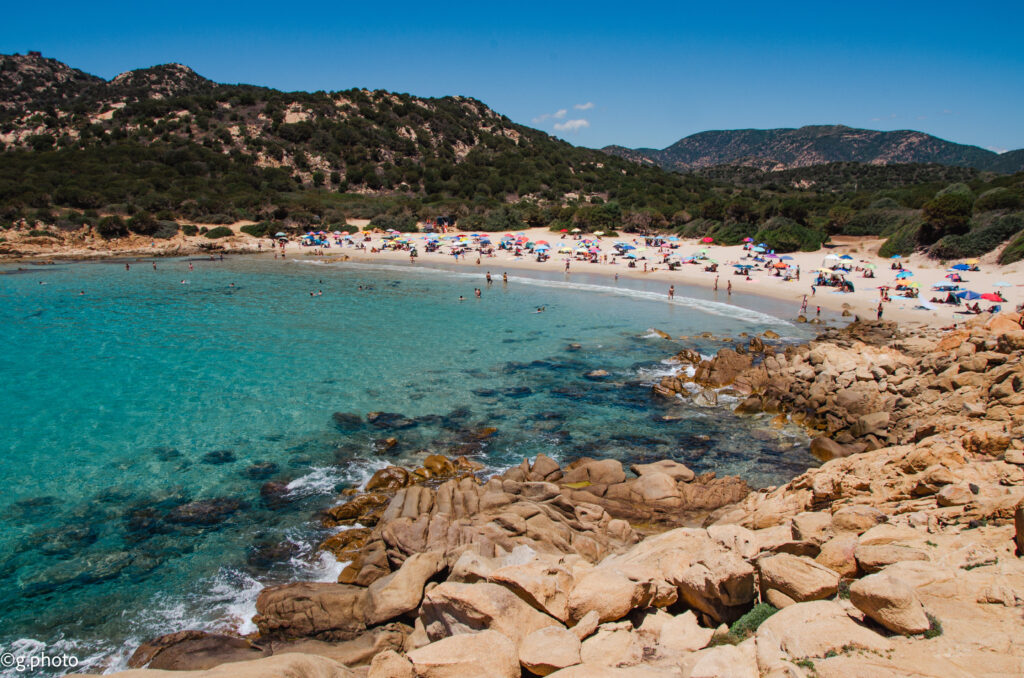 Baia di Su Giudeu vista dagli scogli, spiaggia affollata sullo sfondo